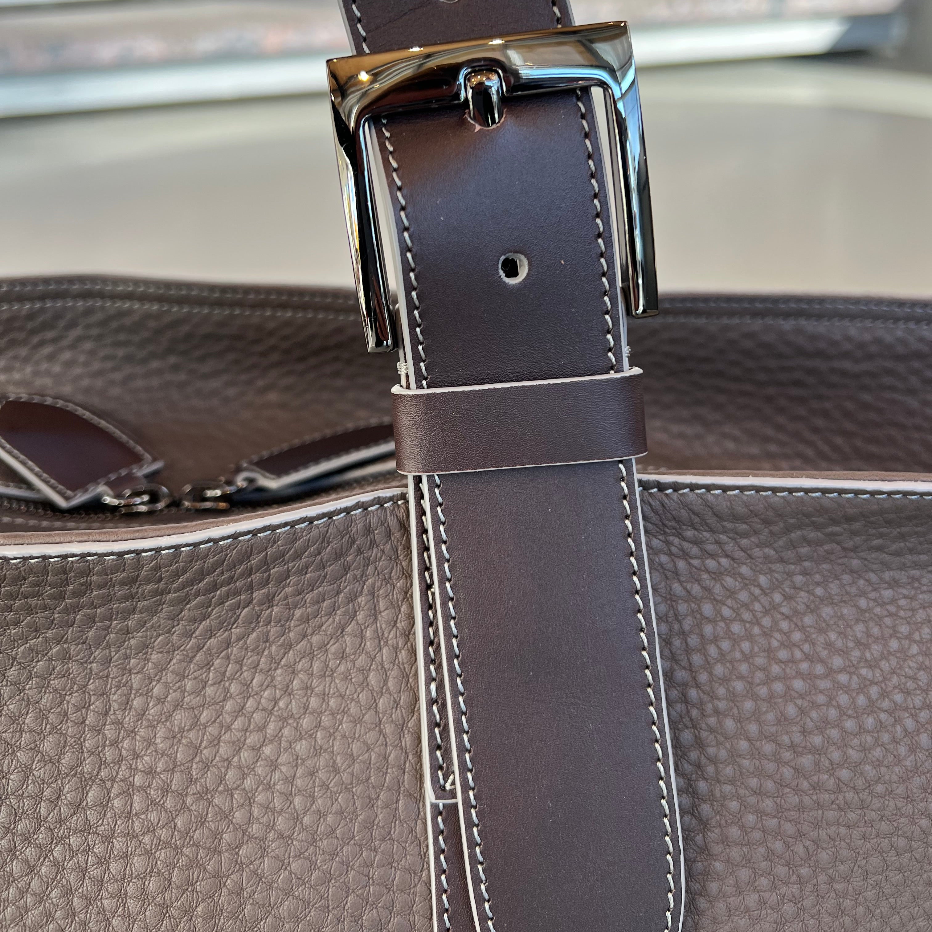 Close-up of a brown leather bag with a metal buckle.
