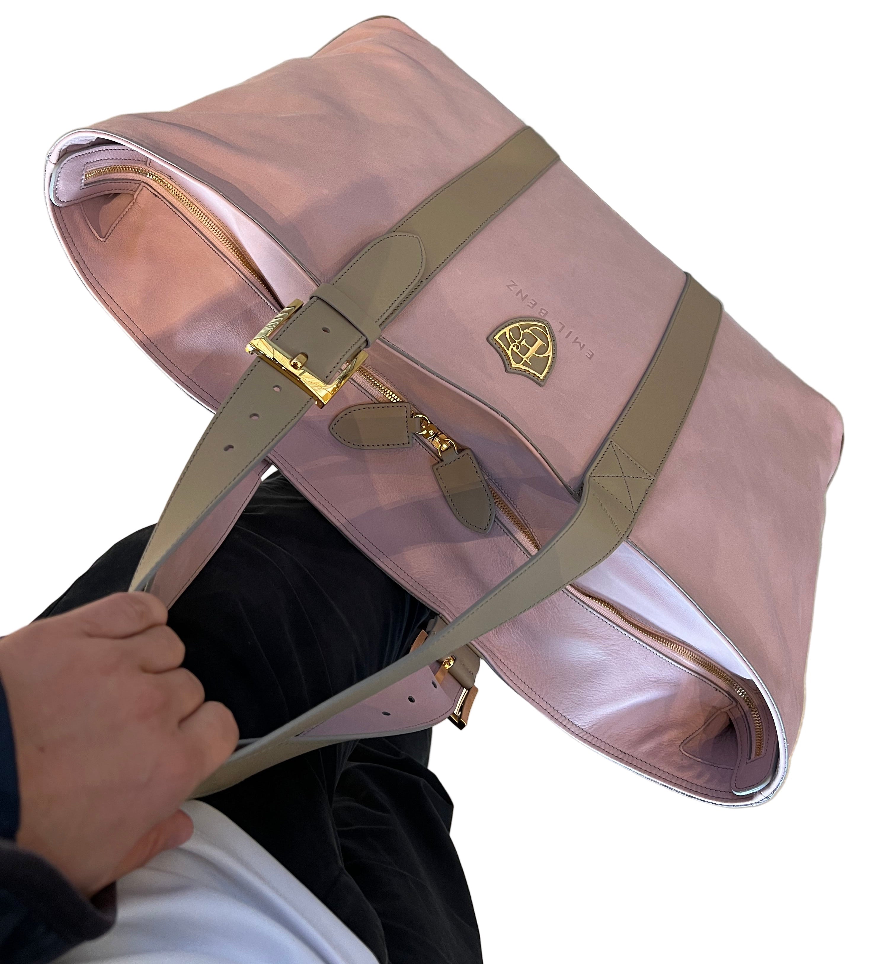 Pink bag with beige strap held by a person against a neutral background